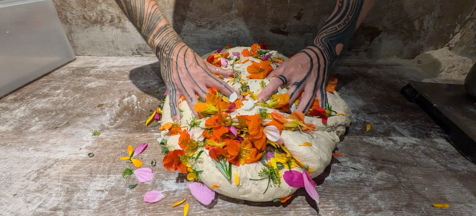 Getatoeeerde handen drukken eetbare bloemen in een zuurdesembrood, Bakkerij Het Lage Woud in Makkinga