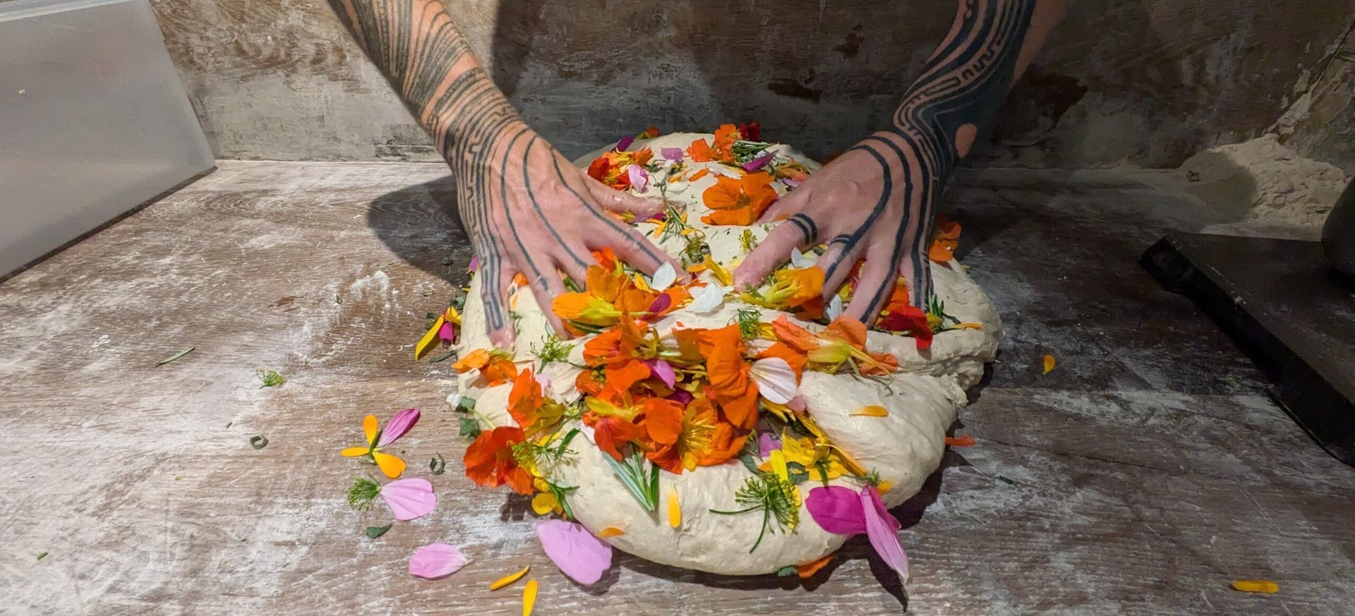 Handen drukken eetbare bloemen in een groot zuurdesemdeeg